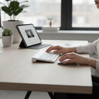 digitaley.co pastel blue wireless keyboard and mouse set on a wooden desk with a tablet in the background.